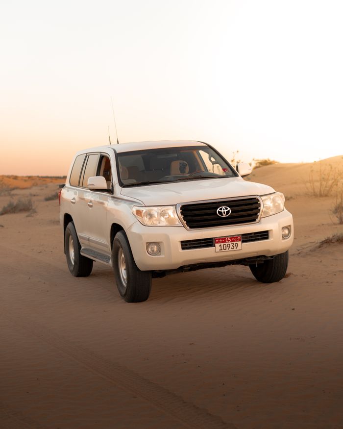 White SUV navigating the sandy desert landscape of Al Sharjah during sunset.