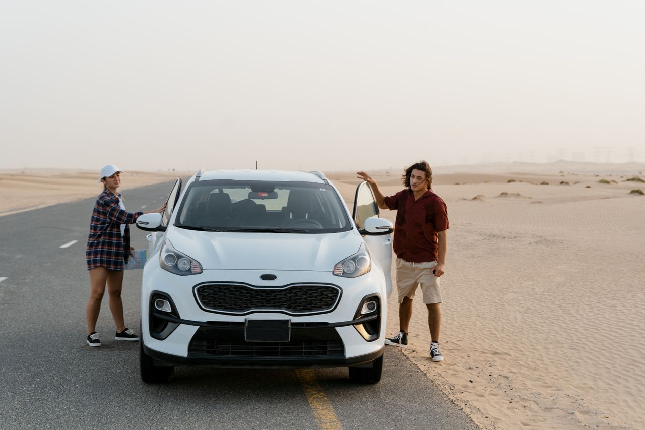 A couple stands by their SUV on a desert road, enjoying a scenic road trip.